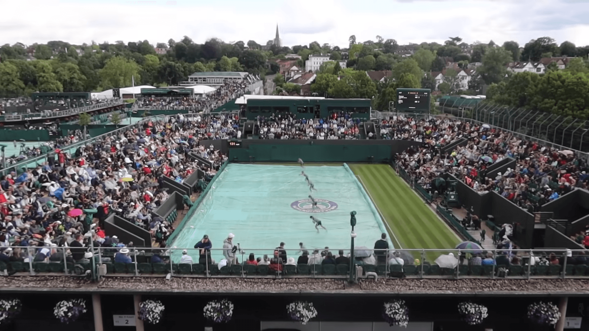 Ground crew removing tarpaulin covers from a Wimbledon court after a rain delay during the 2023 Championships
